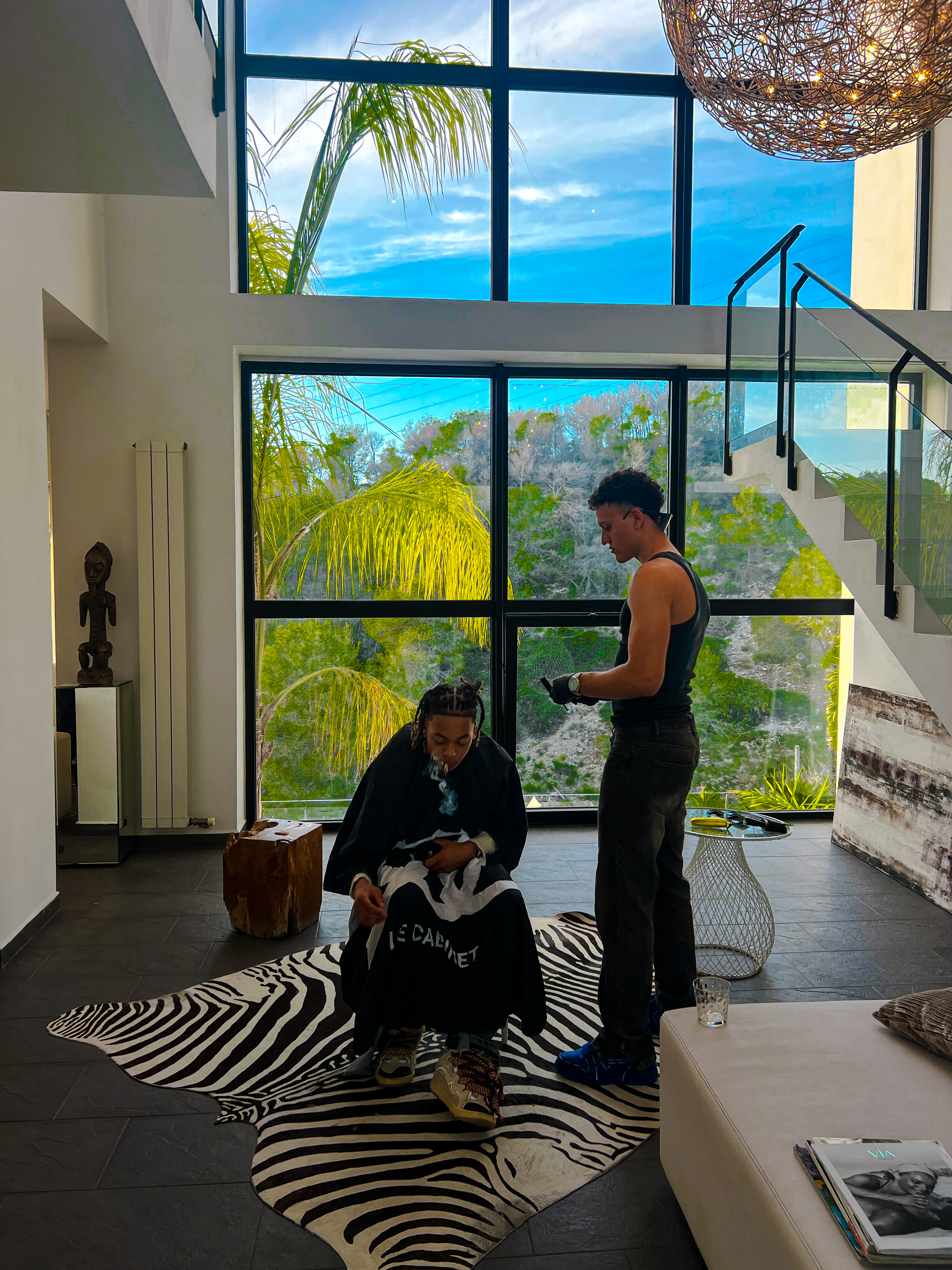 Mehdi travaille les cheveux d'un client devant les grandes fenêtres d'un salon.