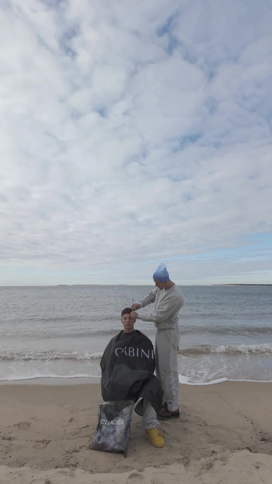 Mehdi coupe les cheveux d’un client face à la mer.